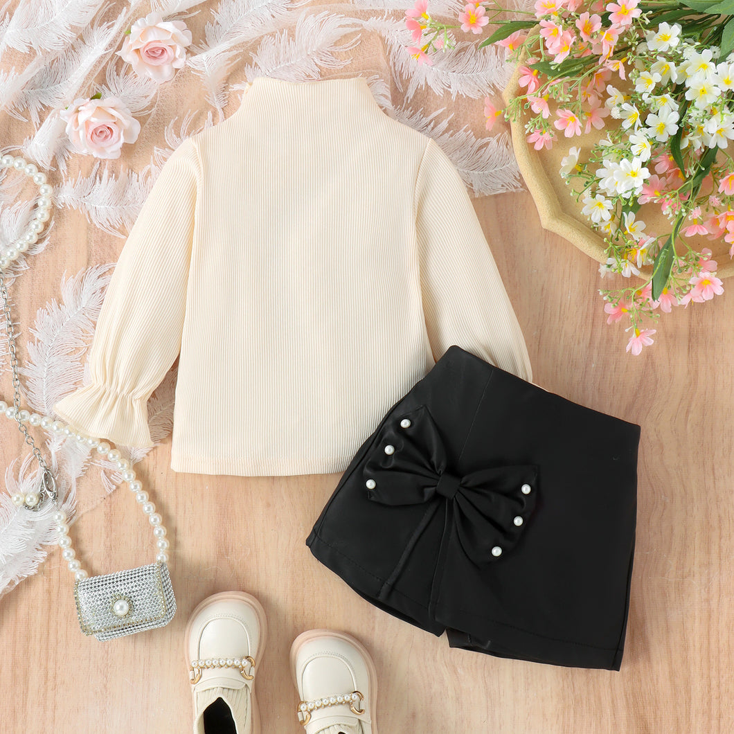 Blusa crema cuello alto y short pollera negra con moño grande